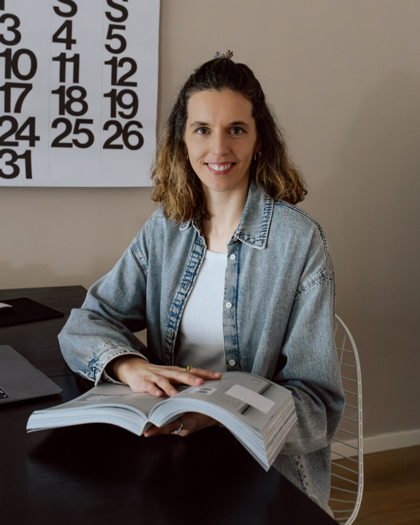 Sibylle Egelkamp, Freelance Grafikdesignerin Berlin, sitzt am Schreibtisch mit aufgeschlagenem Buch — Grafikdesignerin Berlin, Logo & Markenauftritt gestalten lassen