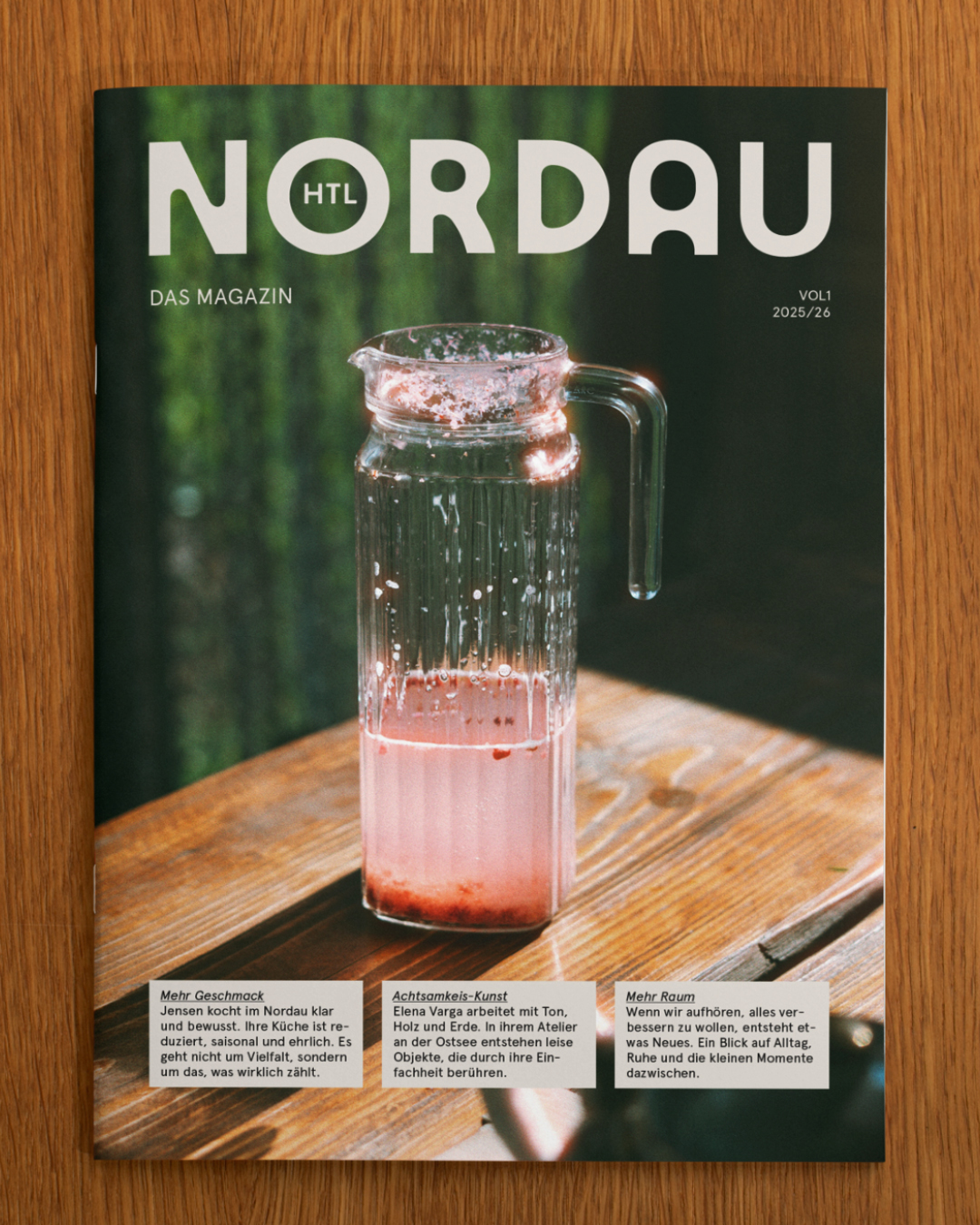 Magazin Nordau liegt auf Holztisch, Glas Karaffe mit rosafarbenem Getränk im Fokus