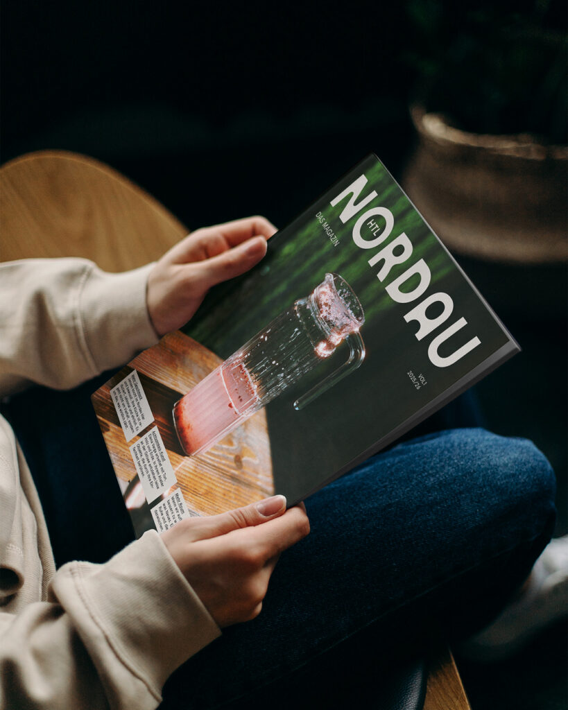 Person sitzt und hält ein aufgeschlagenes Magazin in den Händen, ruhige Lese­situation im Innenraum.